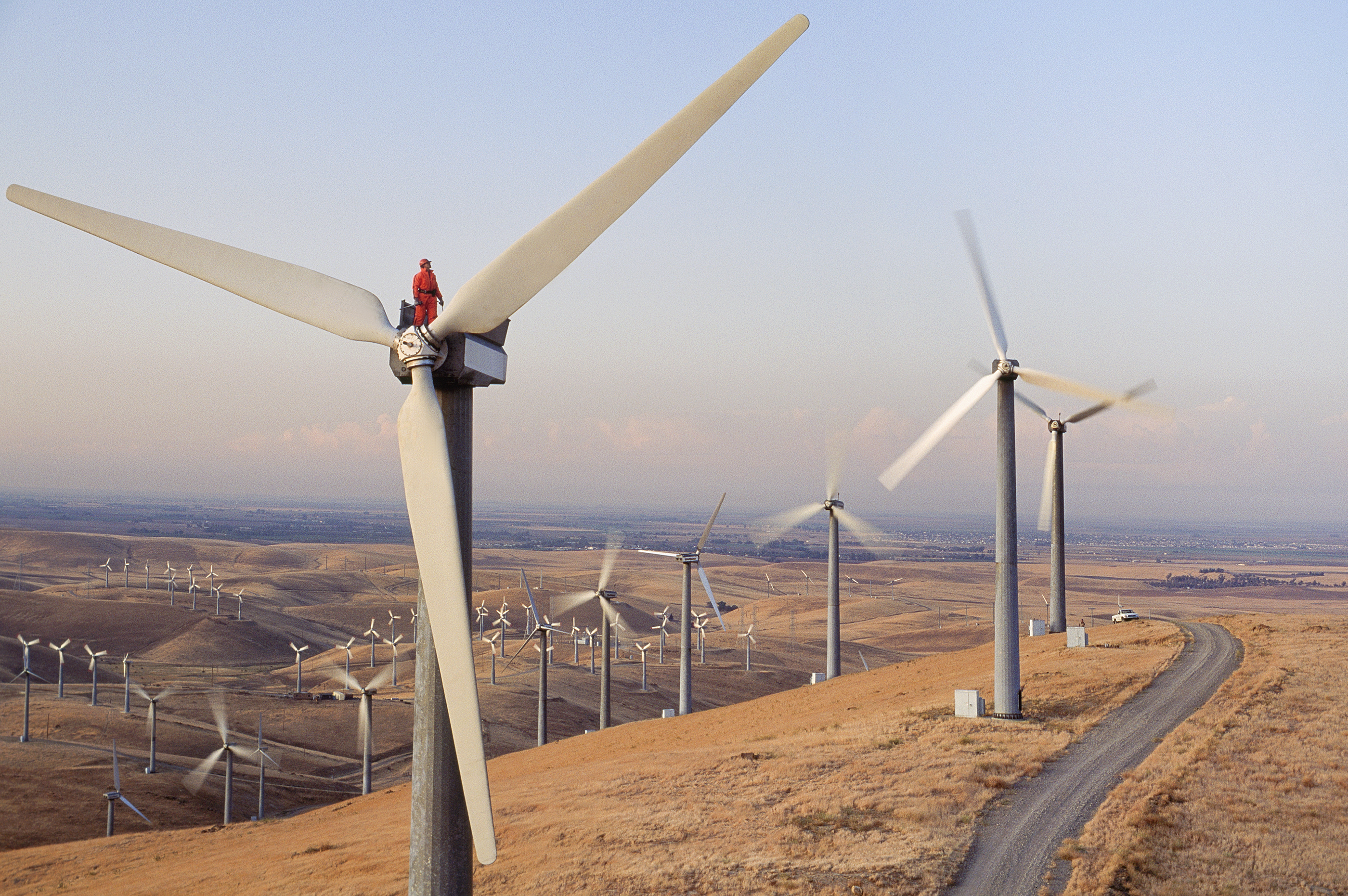 High-angle view of a worker atop a wind turbine in a rural setting.